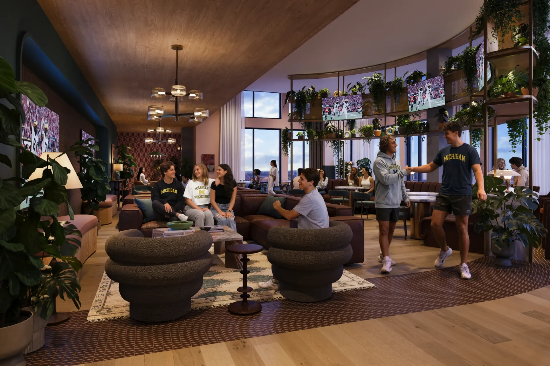 A group of young adults socialize in a modern, open lounge with large windows, plants, and comfortable seating—a welcoming space often found in UMich Off-Campus Housing. Some wear University of Michigan shirts as natural light fills the room.