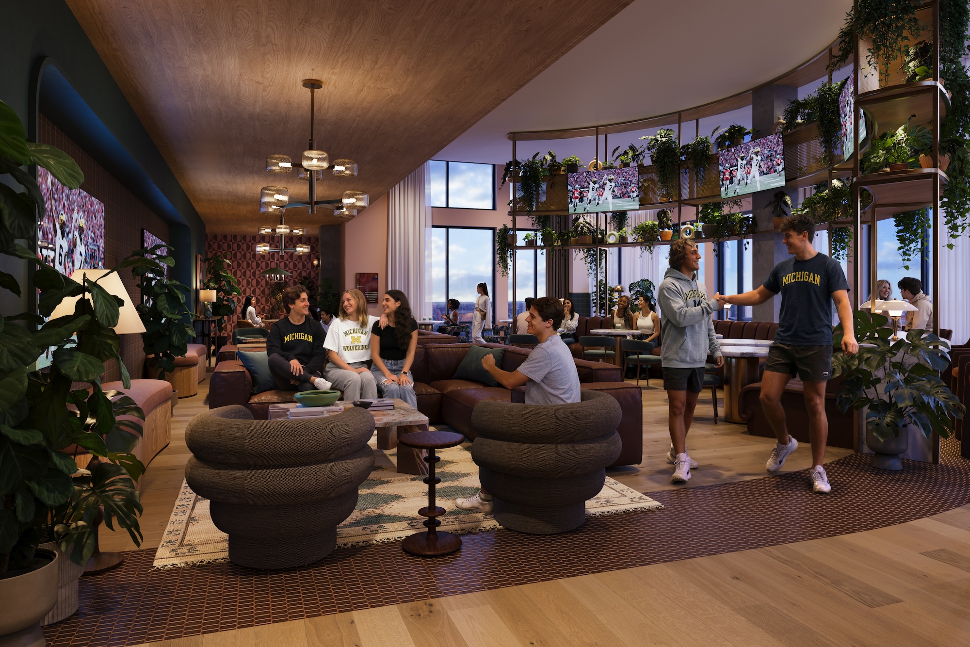 A group of young adults socialize in a stylish, modern UMich Off-Campus Housing lounge with plants, large windows, and cozy seating. Some are seated and talking, while others stand and interact near a curved bookshelf.