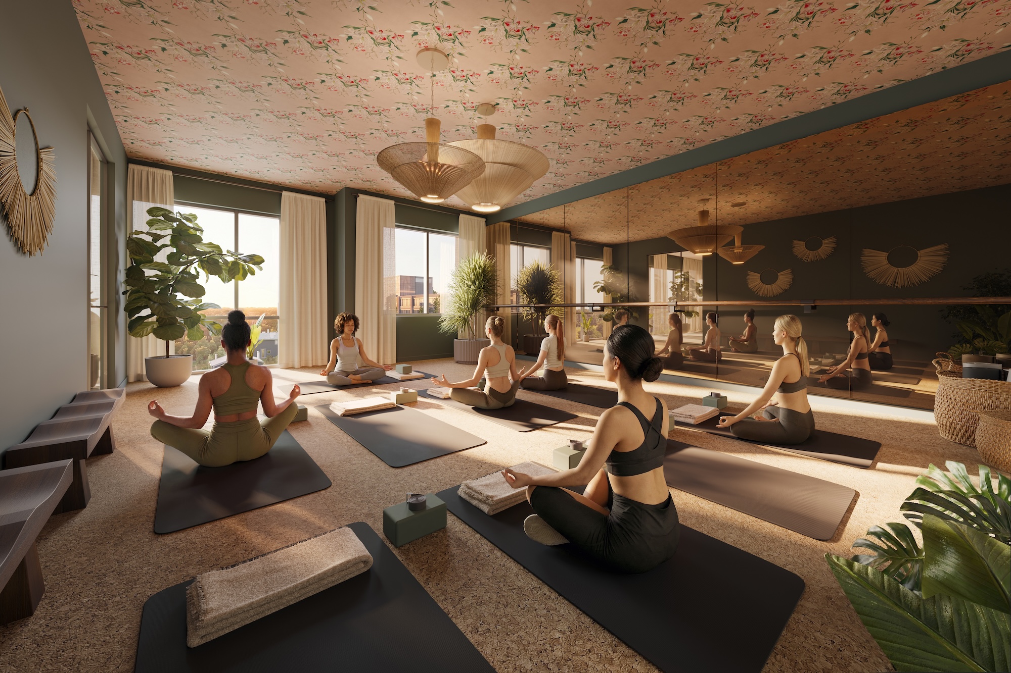 A group of people practice yoga on mats in a bright, modern UMich Off-Campus Housing studio with large windows, plants, and decorative ceiling and mirrors. They are seated in a cross-legged meditation pose facing the instructor.