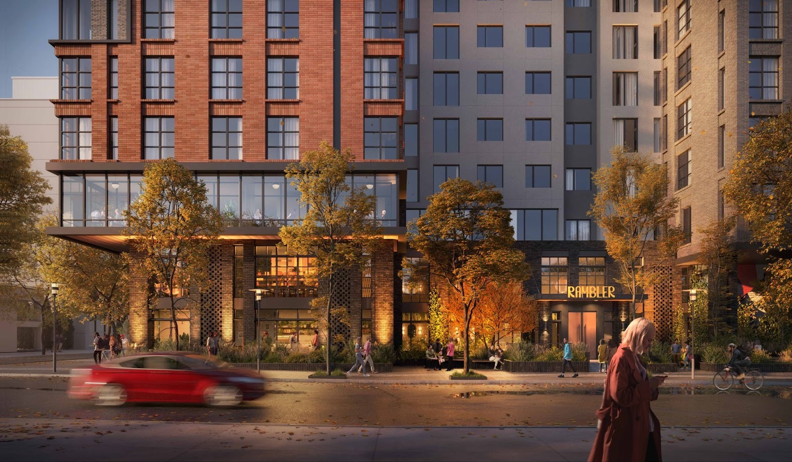 A modern multi-story hotel with large windows, autumn trees lining the sidewalk, people walking, a cyclist, and a red car driving by. The hotel entrance sign reads “Rambler,” near student apartments Ann Arbor. A person in a long coat stands in the foreground.