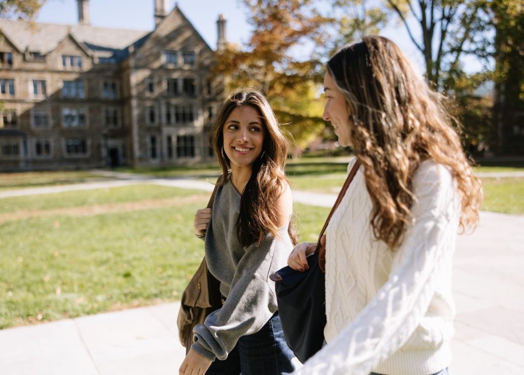 Two UMich students walking together across campus in Ann Arbor on a sunny fall afternoon.