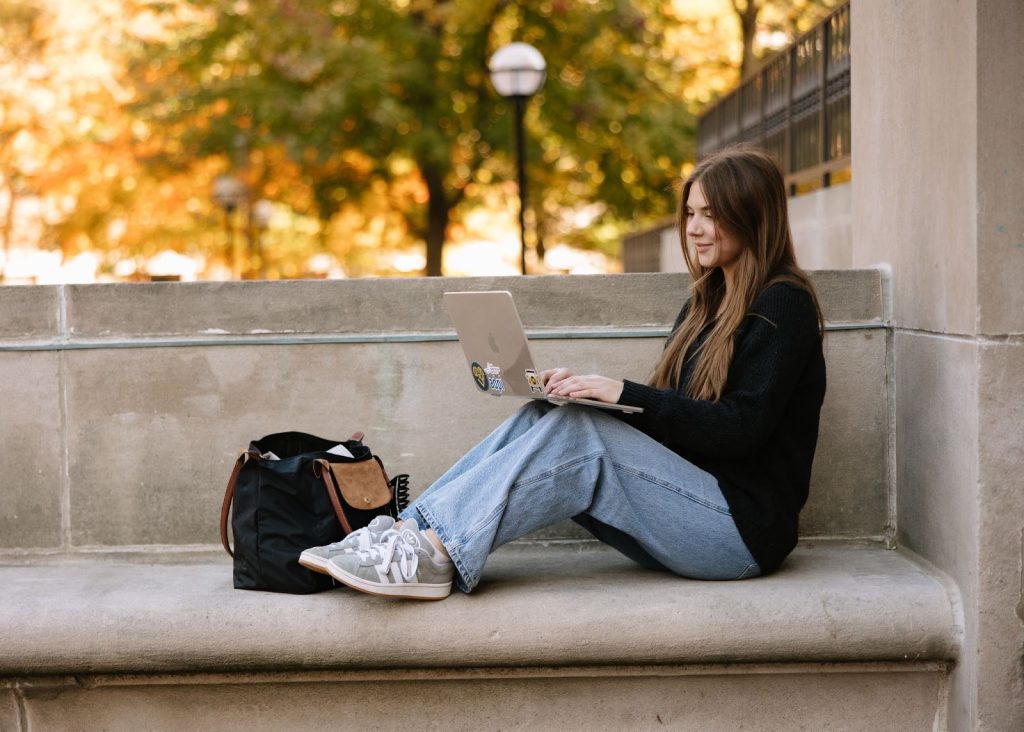 UMich student studying on a laptop outdoors in Ann Arbor during fall, seated near in the Diag.