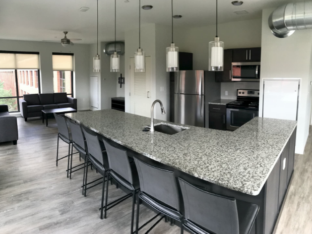 Modern kitchen and living area, featuring stainless steel appliances and furnished living spaces inside of Vic Village North, a student apartment near UMich. 