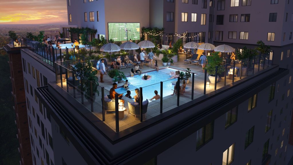 Rooftop pool deck at Rambler Ann Arbor student apartments with hot tub, outdoor lounge seating, and large screen overlooking University of Michigan campus at sunset.