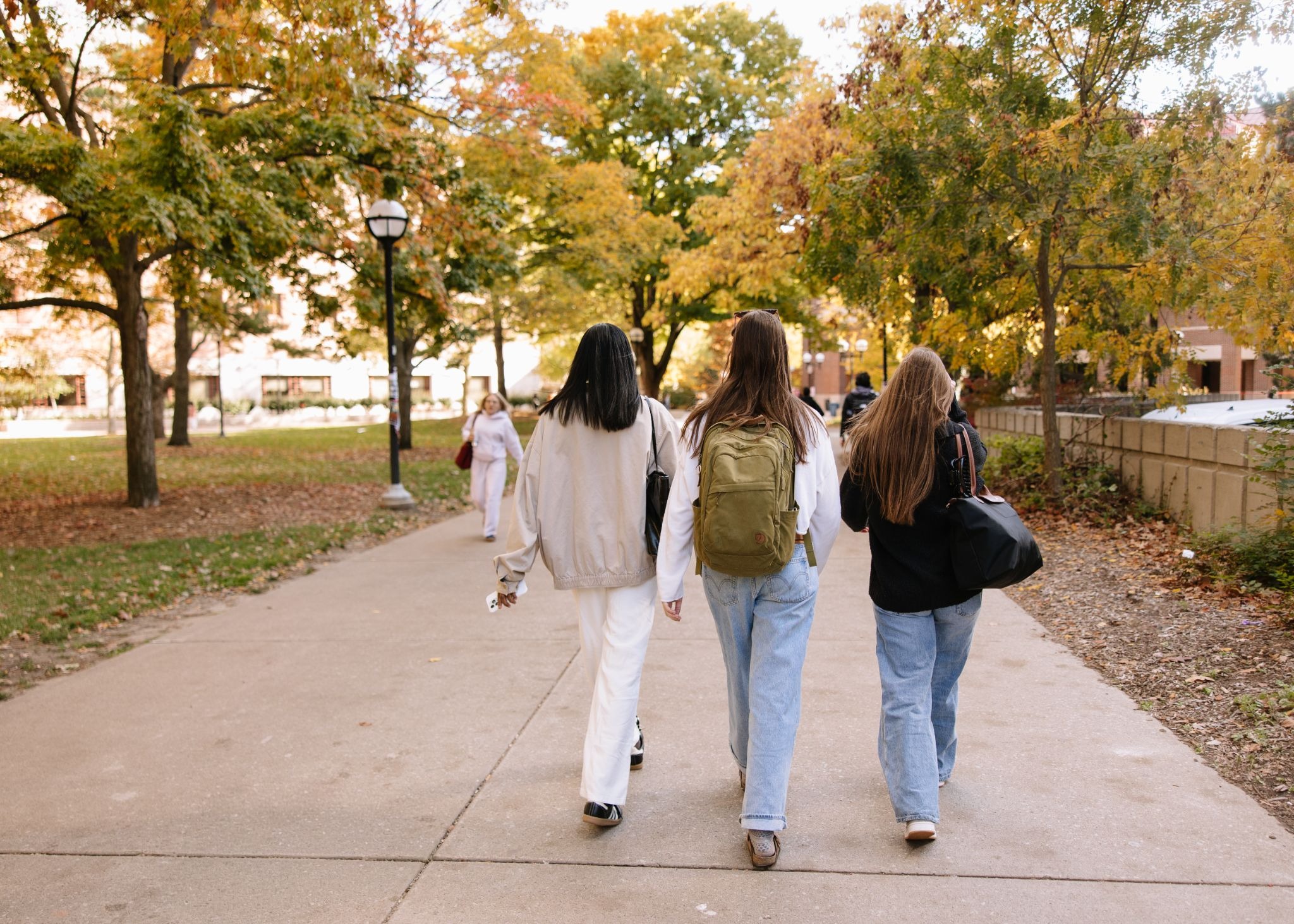 Three UMich students walking through the central campus during fall.