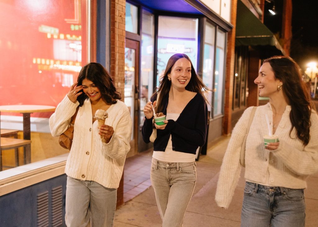 Three UMich students walking on State Street at night while eating ice cream.