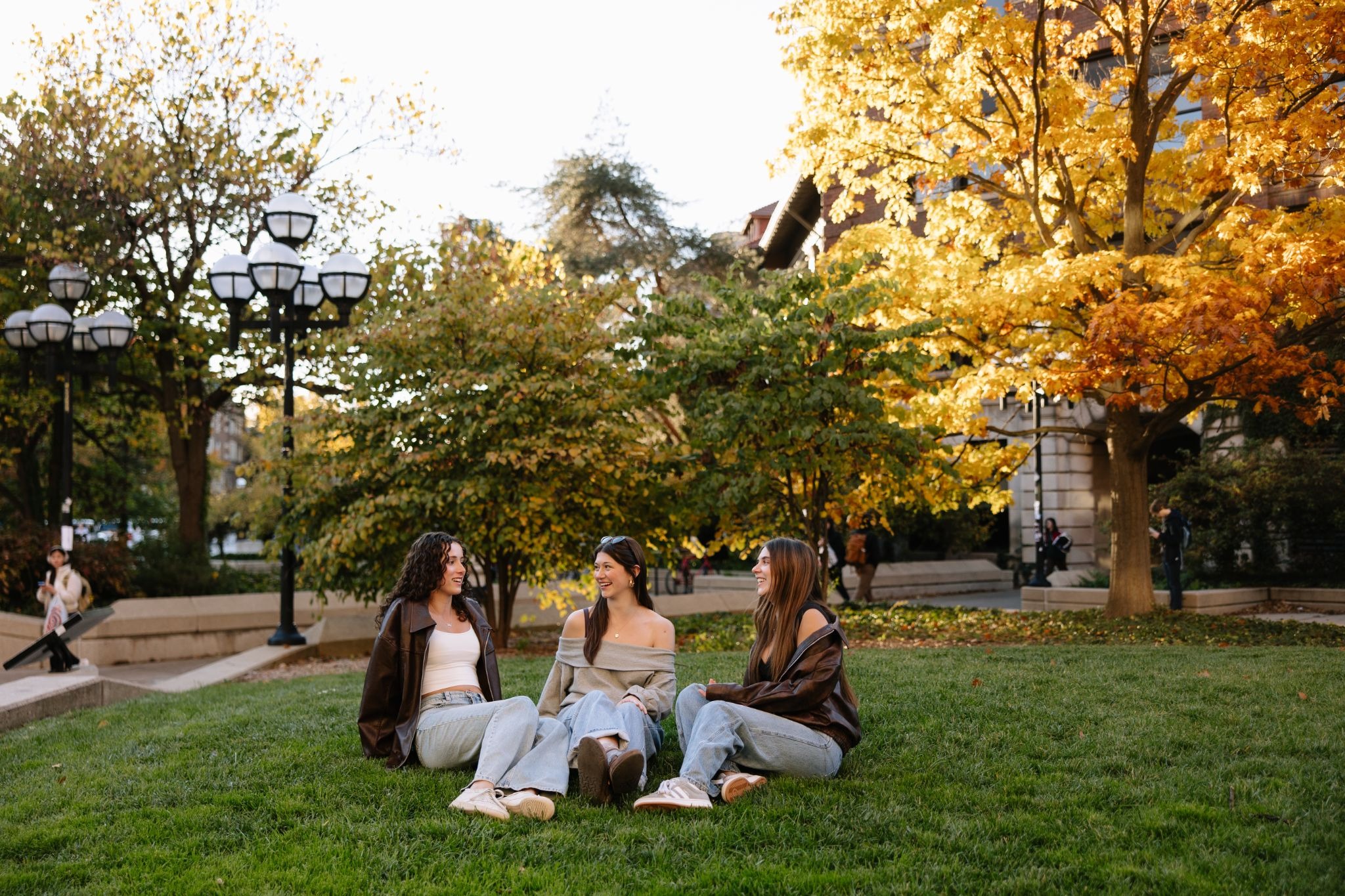 Three UMich students sitting on the grass right outside of the Diag, a central point on the university’s campus.