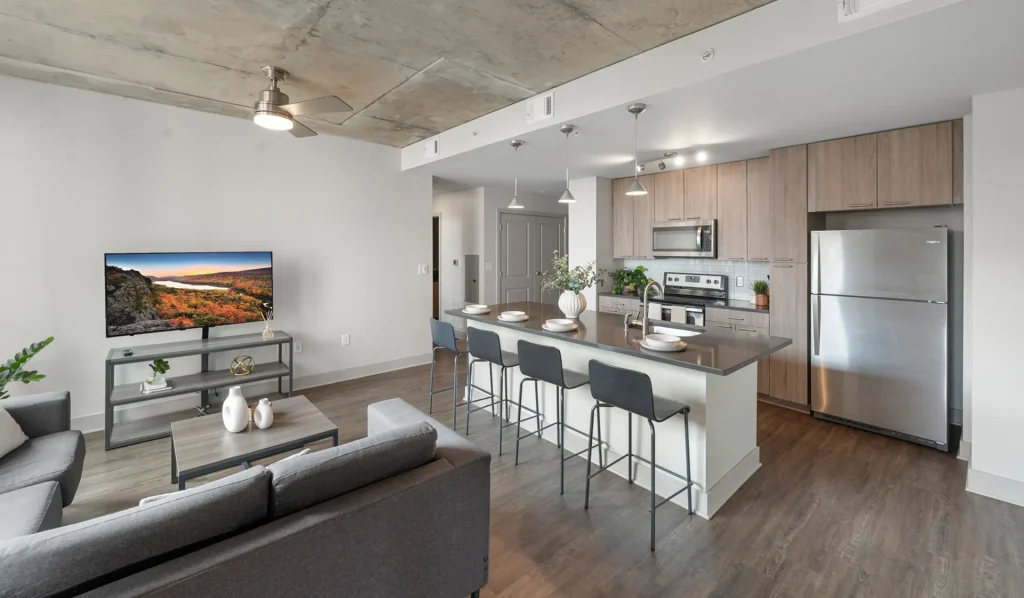 Six11 Ann Arbor apartment interior featuring an open-concept kitchen and living area with island seating and stainless steel appliances.