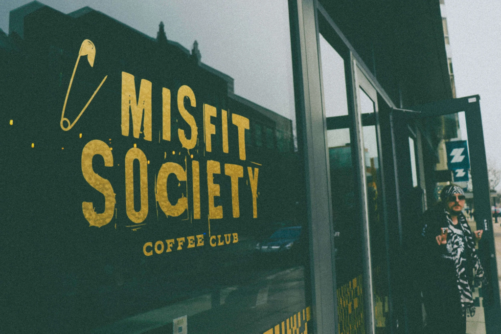 Exterior of Misfits Society Coffee Club in Ann Arbor with bold yellow signage, a trendy café known for creative drinks and a relaxed brunch vibe near the University of Michigan.