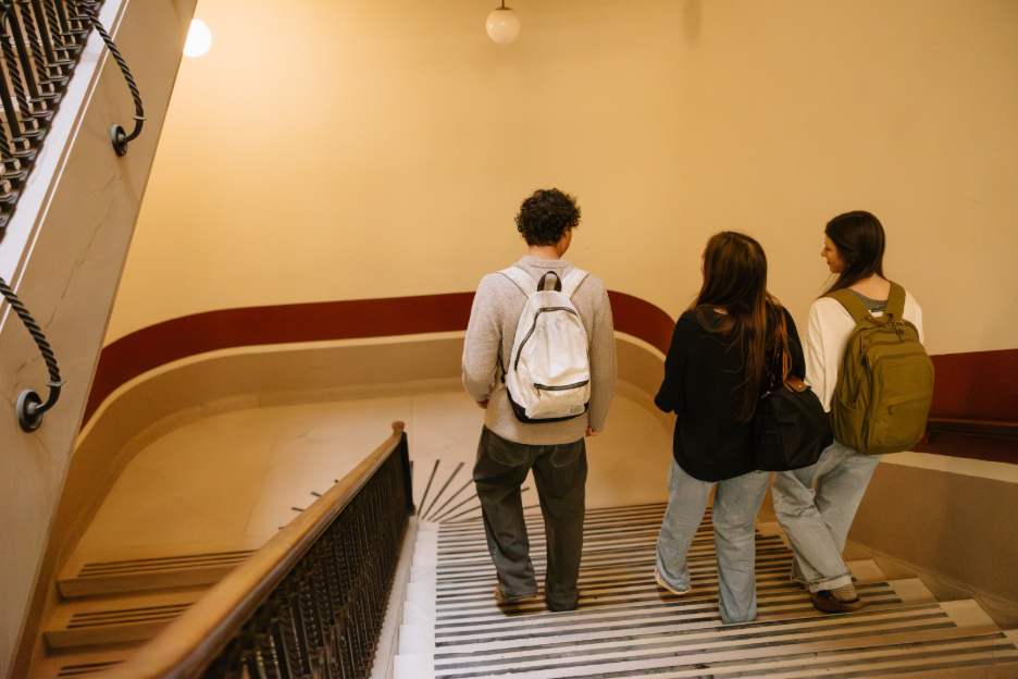 Three UMich students walking down the stairs in the Hatcher Graduate Library, a building located right off the Diag in Ann Arbor.
