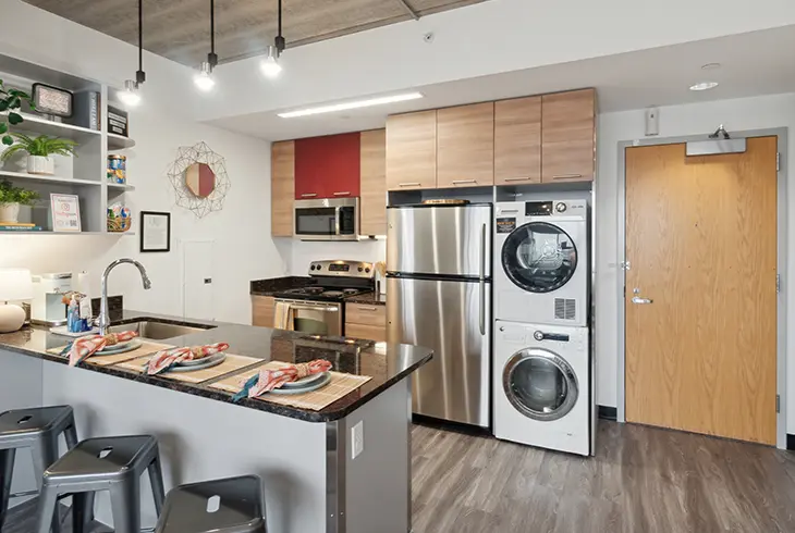 Open-concept kitchen in a Z West Ann Arbor apartment with island seating, stainless steel appliances and stacked washer-dryer.