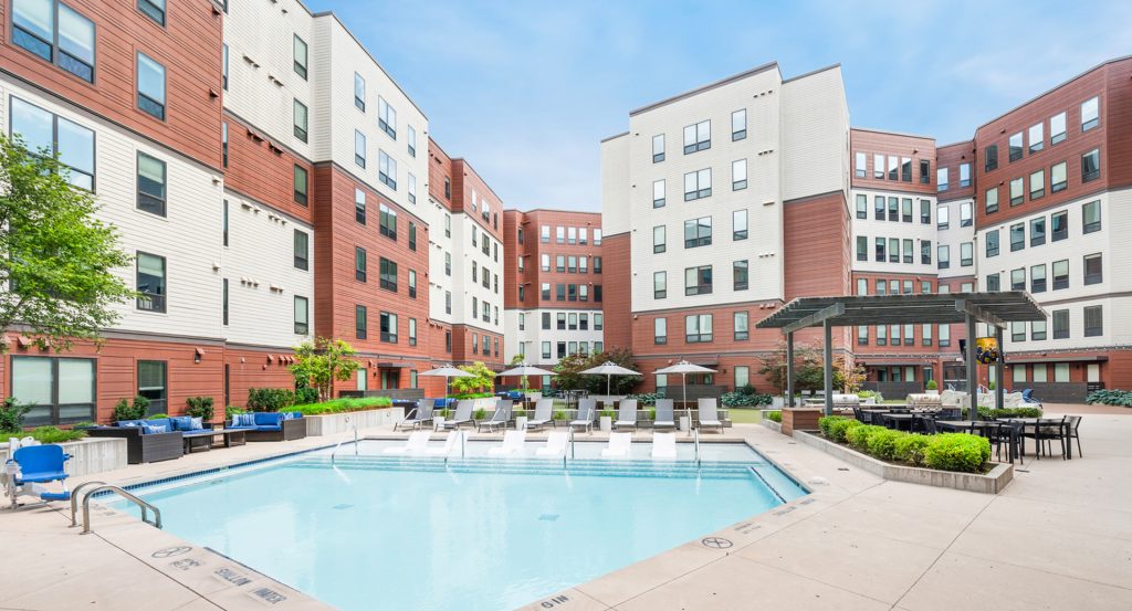  The Yard Ann Arbor outdoor pool deck with lounge chairs, grilling stations, umbrellas and large TV screen, modern student apartments near the University of Michigan.
